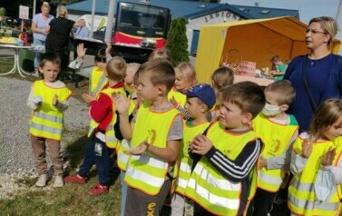 Dzieci ubrane są w bluzy i kamizeli odblaskowe. Stoją. Biją brawo. Za nimi stoi nauczycielka.