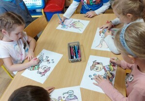 Dzieci siedzą przy stolikach. Kolorują obrazki związane z myciem się.