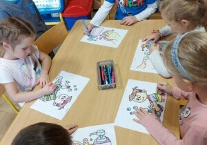 Dzieci siedzą przy stoliku. Kolorują obrazki związane z Dniem Czyścioszka