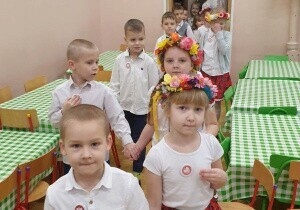 Dzieci odświętnie ubrane idą w parach. Są na jadalni. Dziewczynki na głowach mają wianki.