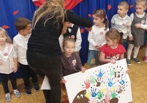 Dzieci ubrane są na galowow. Dw&oacute;jka dzieci stoi z przodu. Trzymaja w rękach prace plastyczną. 
