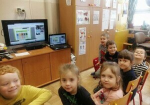 Dzieci siedzą na krzesełkach przed telewizorem. Oglądają prezentację multimedialną o ekologii.