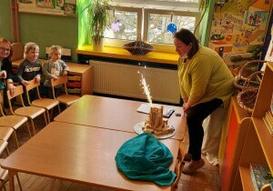 Dzieci odgrodzone są krzesłkami. Na stolikach nauczycielka wykonuje eksperyment. Dzieci przyglądają się.