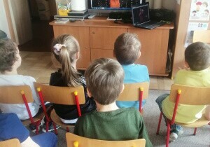 Dziecisiedzą na krzesełkach przed telewizorem w sali przedszkolnej. Oglądają koncert Pana Witka pod tytułem Dylu, dylu.