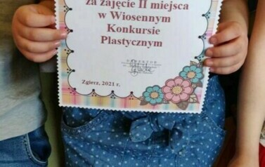 Dziewczynka trzyma w rękach dyplom za udział w konkursie.
