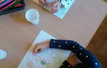 Dzieci siedzą przy stoliku. Kolorują kropki na kartce.