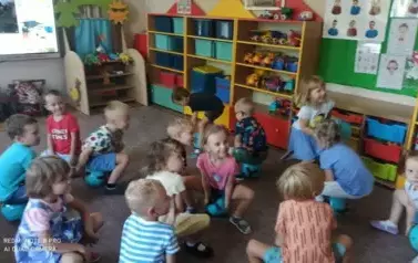 Dzieci siedzą na piłkach. Uśmiechają się.