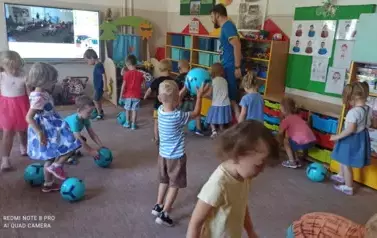 Dzieci chodzą po sali przedszkolnej z piłkami. Turlają, kopią.