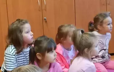 Dzieci siedzą w bibliotece na dywanie. Są zapatrzone.