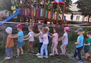 Dzieci stoją w ogrodzie przedszkolnym jeden za drugim.