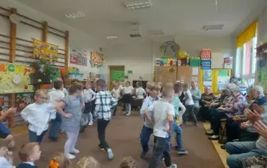 Dzieci ubrane odświętnie tańczą taniec Trojak na środku sali. Goście klaszczą.