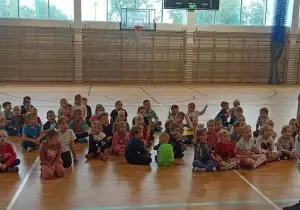 Dzieci siedzą na sali gimnastycznej. Czekają.