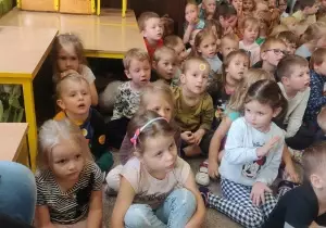 Dzieci siedzą na dywanie. Oglądają przedstawienie teatralne.