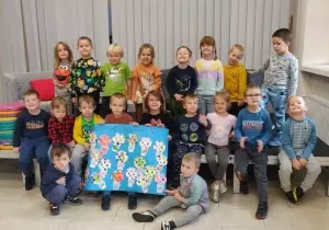 Zdjęcie grupowe dzieci w bibliotece. Dzieci trzymają w rękach plakat.