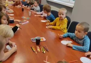 Dzieci siedzą przy stole. Kolorują kolorowankę baloniki.