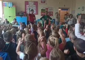 Dzieci stoją tyłem. Trzymają ręce w g&oacute;rze. Przed nimi stoi dw&oacute;ch pan&oacute;w. Jeden z nich tańczy.