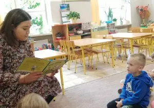 Dzieci siedzą na dywanie w siadzie skrzyżnym. Słuchają opowiadania czytanego przez mamę Zosi.