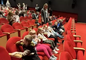 Dzieci siedzą w fotelach teatralnych. Są elegancko ubrane.