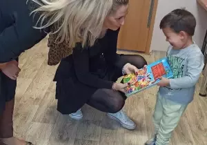 Nauczycielka wręcza nagrodę chłopcu w bibliotece przedszkolnej.