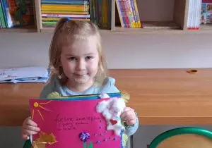 Dziewczynka trzyma w ręku nagrodę, książkę. Uśmiecha się do zdjęcia.