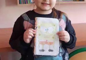 Dziewczynka trzyma w ręku nagrodę, książkę. Uśmiecha się do zdjęcia.