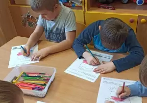 Dzieci siedzą przy stoliku. Kolorują obrazek mapa Polski.