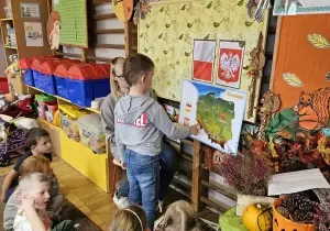 Chłopiec podchodzi do mapy Polski. Mapa Polski przywieszona jest do tablicy.