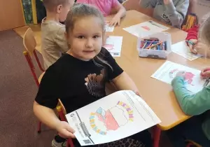 Dziewczynka pokazuje prace plastyczną.