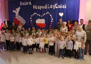 Zdjęcie grupowe przedszkolak&oacute;w na sali. Dzieci są odświętnie ubrane. Przypięte mają kotyliony.