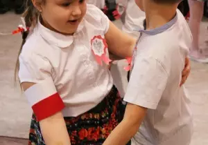 Dziewczynka z chłopcem tańczą. Są odświętnie ubrani.