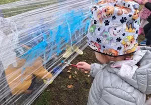 Dziewczynka maluje pędzlem po streczu.