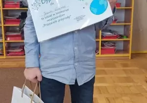 Chłopiec trzyma w ręku dyplom i nagrodę. Uśmiecha się do zdjęcia.