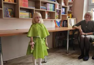 Dziewczynka stoi na środku. Ubrana jest na zielono. Recytuje wiersz.