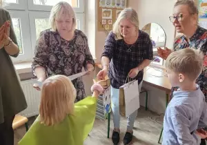 Pani Dyrektor trzyma w ręku dyplom. Nauczycielka podaje dziewczynce nagrodę. Obok stoi chłopiec.