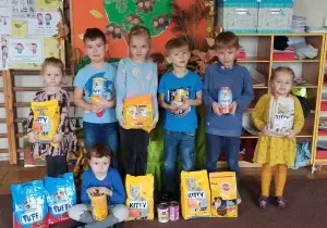Zdjęcie grupowe dzieci w sali przedszkolnej. Dzieci trzymają w rękach karmę dla psow i kot&oacute;w.