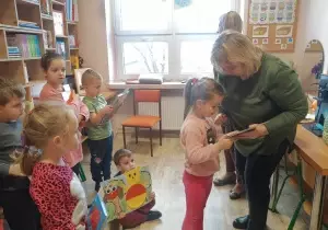 Pani Dyrektor wręcza książkę dziewczynce. Dzieci stoją z tyłu. Przyglądają się.