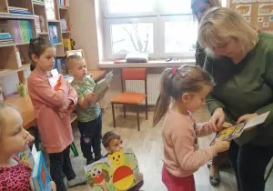 Pani Dyrektor wręcza książkę dziewczynce. Dzieci stoją z tyłu. Przyglądają się.