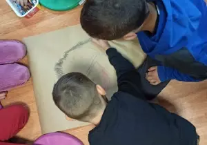 Dw&oacute;ch chłopc&oacute;w wsp&oacute;lnie rysuje obrazke na dużym kartonie.