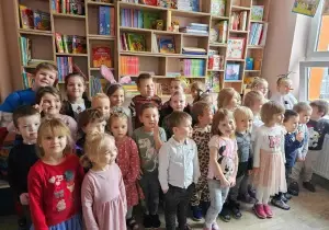 Dzieci stoją w bibliotece przedszkolnej. Uśmiechają się do zdjęcia.