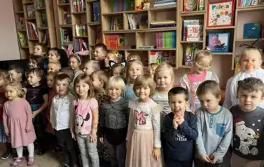 Dzieci stoją w bibliotece przedszkolnej. Uśmiechają się do zdjęcia.