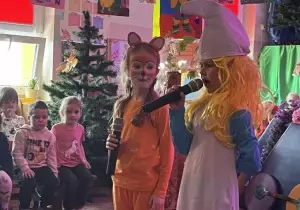 Dziewczynka przebrana za smerfetkę m&oacute;wi przez mikrofon. Obok stoi dziewczynka przebrana za klakiera.