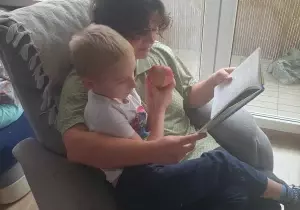 Mama czyta synkowi książkę. Siedzą w fotelu w domu.