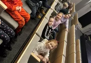 Dzieci uśmiechają się do zdjęcia. Siedzą w fotelach w kinie.