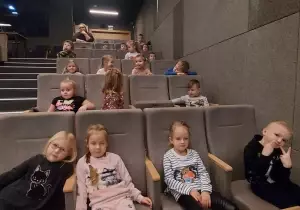 Dzieci siedzą w fotelach kinowych. Uśmiechają się.