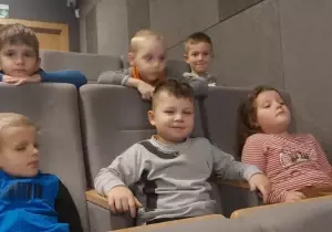 Dzieci siedzą w fotelach kinowych. Uśmiechają się.