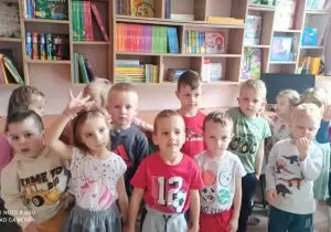 Dzieci stoją w bibliotece przedszkolnej. Uśmiechają się do zdjęcia.