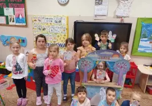 Dzieci stoją w sali przedszkolnej. W rękach trzymają wykonane przez siebie figurki. Dzieci stoją przy teatrzyku.