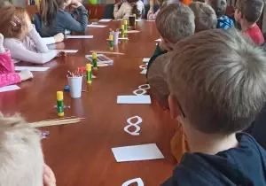 Dzieci siedzą przy długim stole. Oglądają film edukacyjny.
