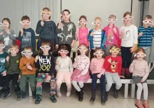 Zdjęcie grupowe dzieci w bibliotece. Każde dziecko zakrywa twarz maską karnawałową.