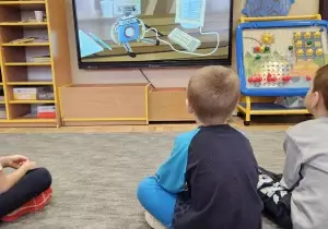 Dzieci siedzą przed tablicą multimedialną. Oglądają edukacyjny film.